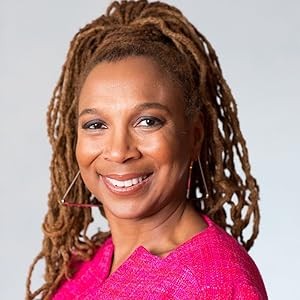 Kimberlé Crenshaw é uma mulher negra madura. Usa camiseta rosa-choque, brincos triangulares, tranças marrom-claras presas em um rabo de cavalo alto e sorri para a foto